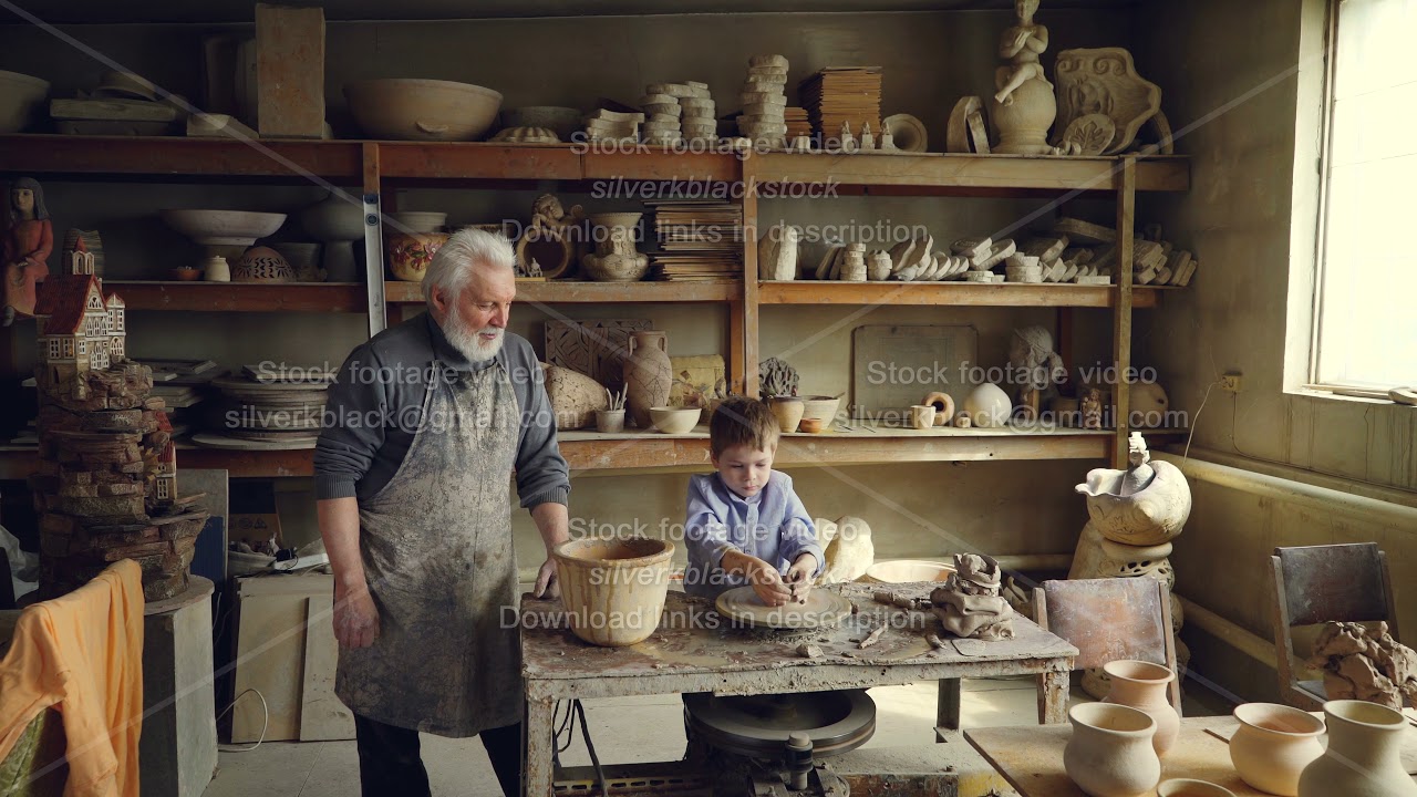 Young grandson is molding clayware in his grandfathers's studio while his loving senior grandpa is
