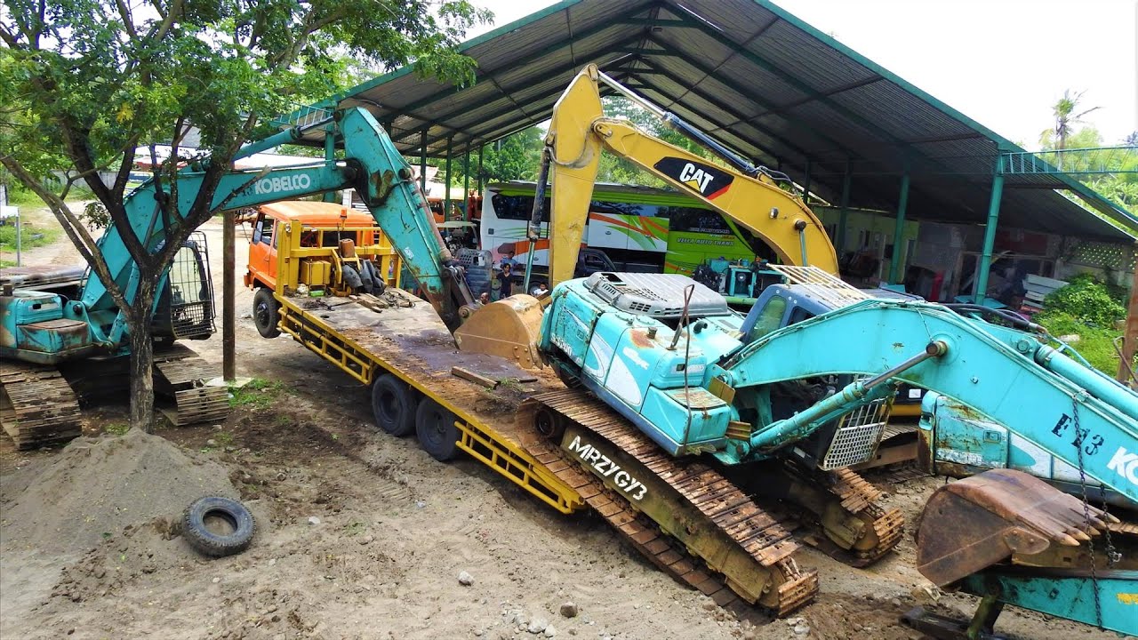 Self Loader Trucks Unloading The Broken Down Excavator Kobelco SK200 CAT 320D