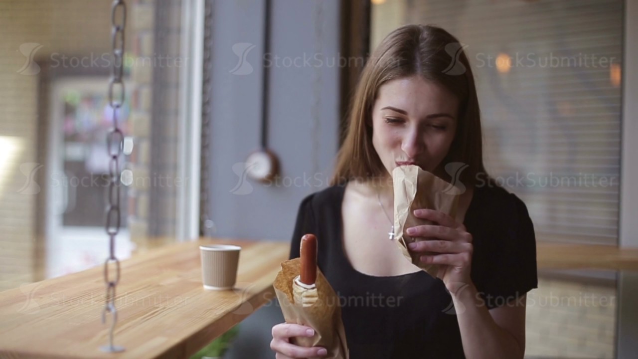 Beautiful girl eating a hot dog in a cafe.