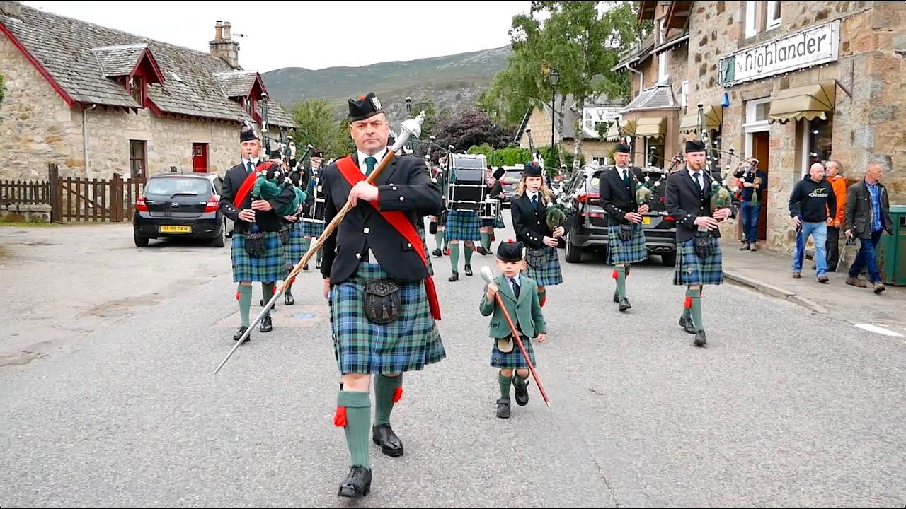 Drum Major Ian Esson has help leading Ballater & District Pipe Band through Braemar, Scotland, 2019