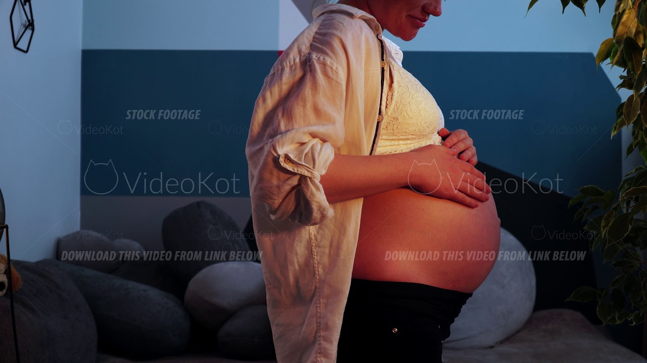 Young pregnant woman is stroking her bare belly with hands and smiling