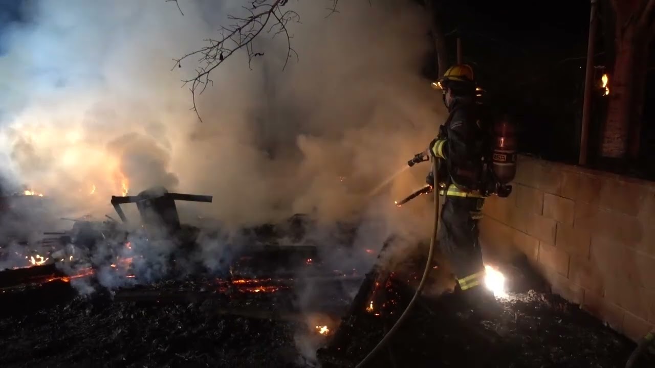 Shed on fire in wooded area.