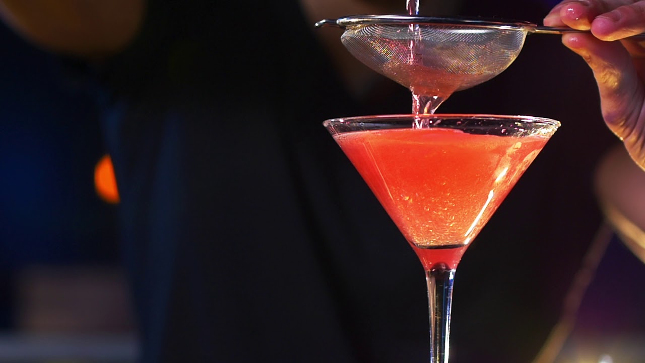 male bartender in background pouring cocktail drin C3CVUHF