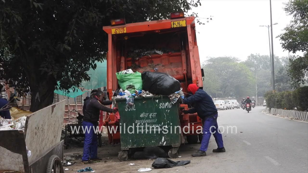 Municipal workers load waste into a hydraulic garbage truck in Delhi