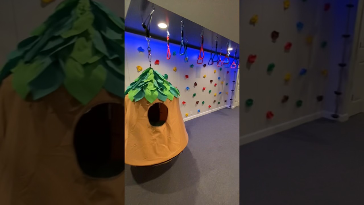 Home jungle gym in the kids&rsquo; playroom with a rock wall, hanging chair, monkey bars, and rope ladder!