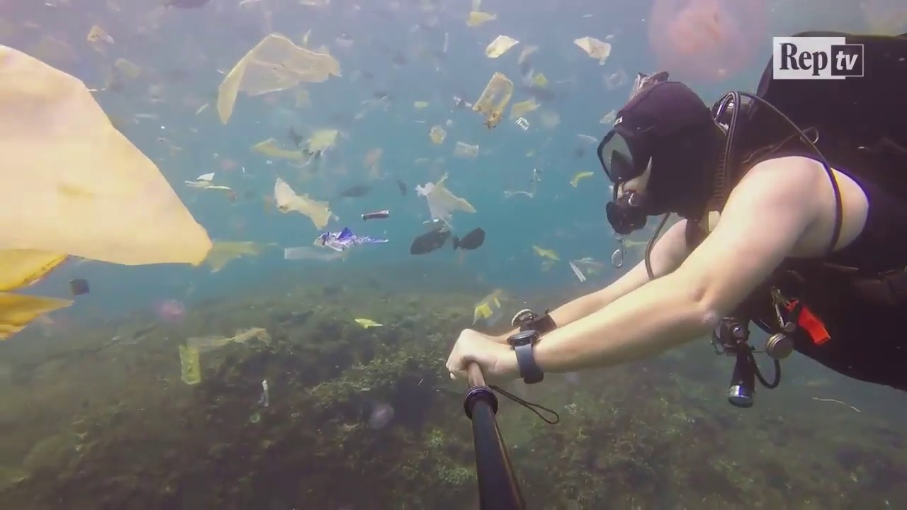 Buceador nada en el mar de indonesia rodeado de desechos de plástico.