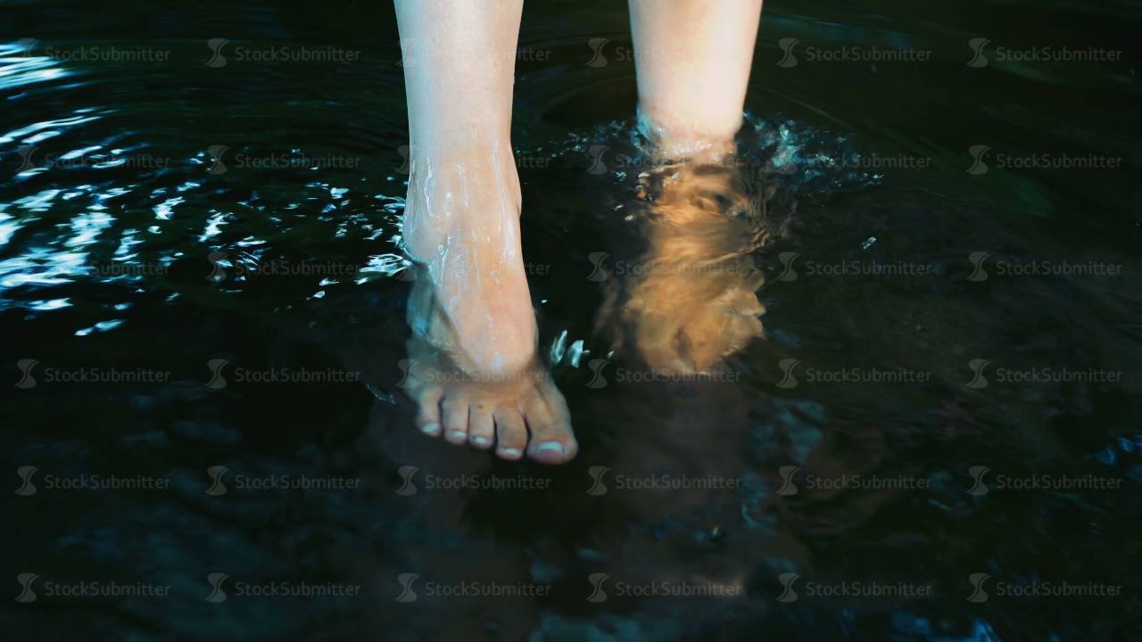 Young girl splashing his feet in the water. Playing in a small river