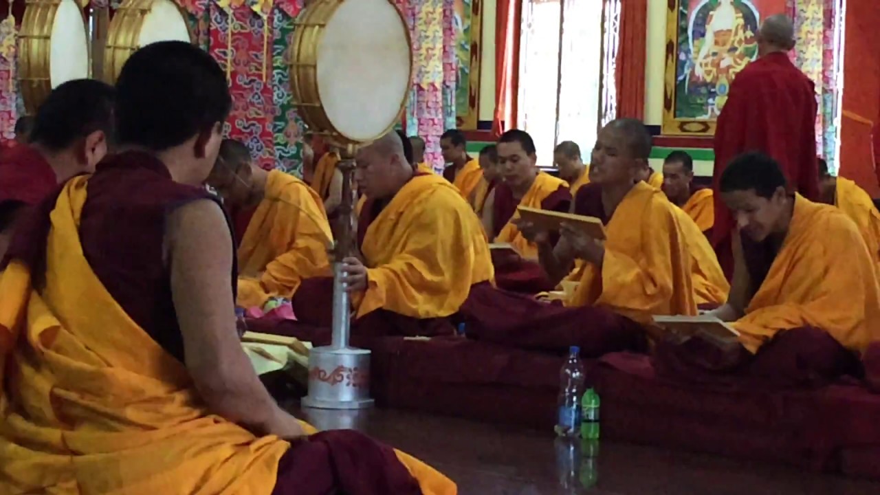 Monks at Gaden Shartse Monastery chanting and playing drums in a Tibetan Buddhist prayer ceremony.