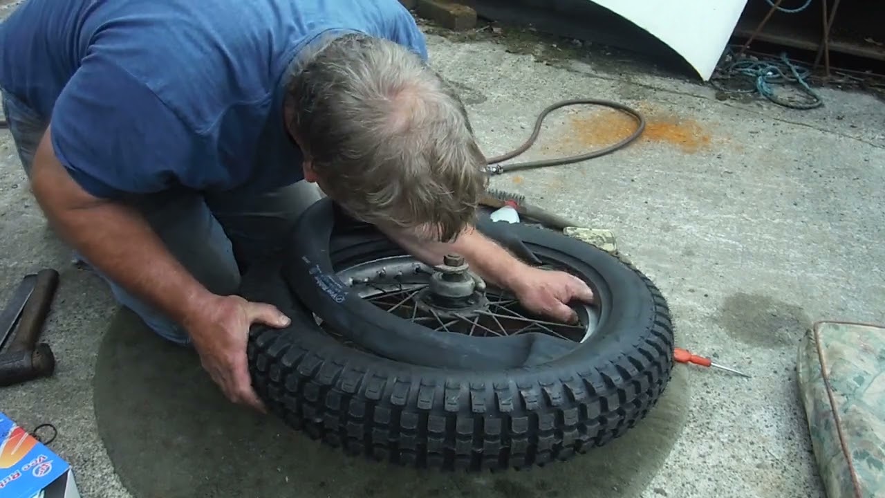 Fitting a new motorcycle tyre to a wheel with badly spaced security bolts.