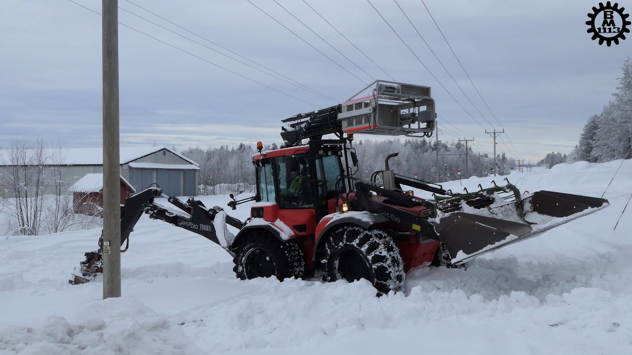 Huddig backhoe loader works with electricity poles in snowy terrain