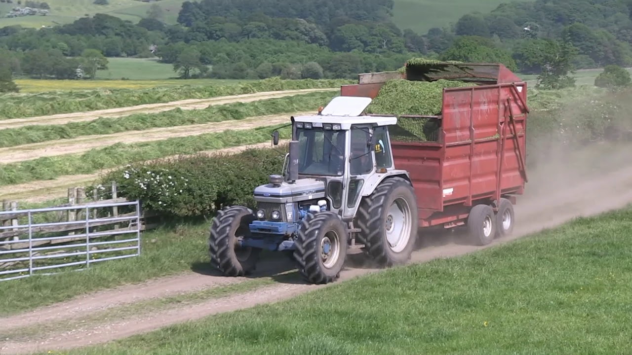 TWO FORD 7810 III SILVER JUBILEE TRACTORS CARTING GRASS