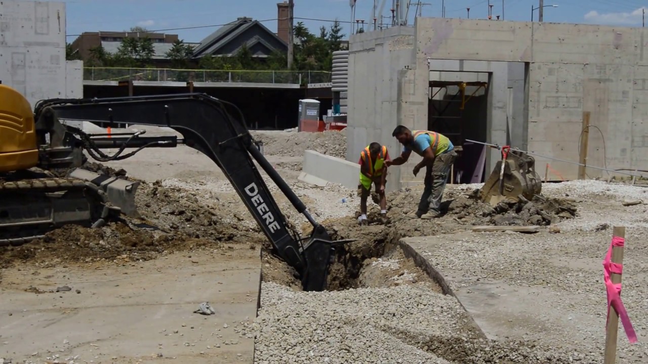 Excavator digging deep enough that a helper is giving hand signals