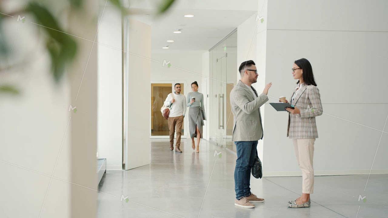 Businesspeople talking and walking indoors in light office building corridor