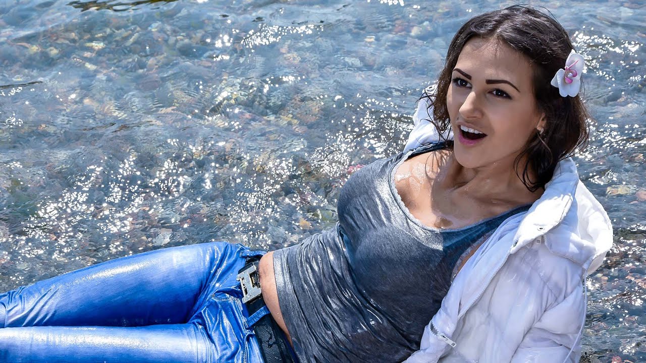 A SLIM MODEL IN A WARM WET JACKET AND JEANS POSE BRIGHTLY ON THE BEACH BY THE SEA FOR WETLOOK VIDEO