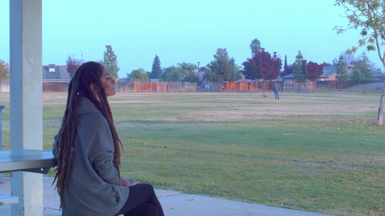Smiling young white rasta girl with dreadlock sitting in a cold public park alone and happy thoughts