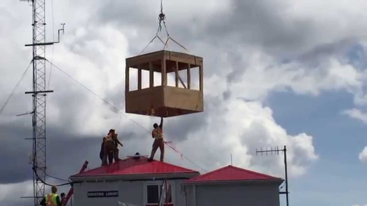 Helicopter delivering a new cupola to a fire lookout on the top of a mountain.