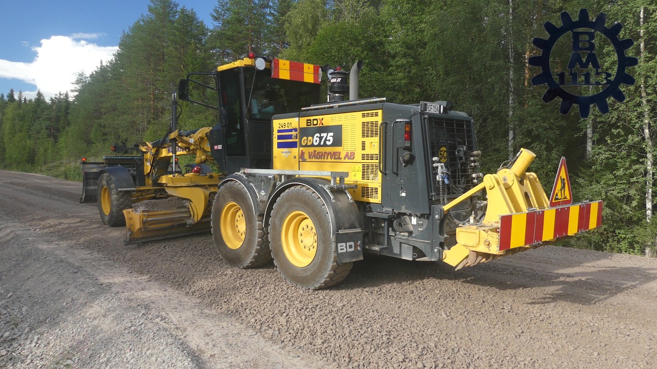 Komatsu GD675 grader and Scania & Volvo trucks spreading gravel on a road