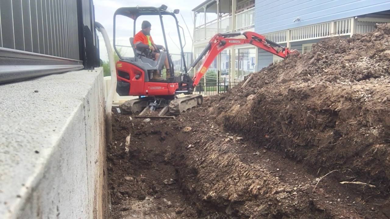 Mini Excavator Digger Digging out behind retaining wall