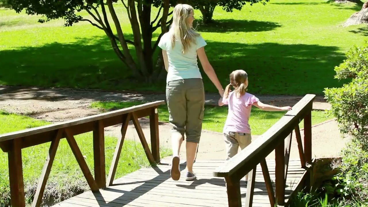 Mother and Daughter Walking Hand in Hand on Wooden Bridge in Park Video | WaveBreak Media