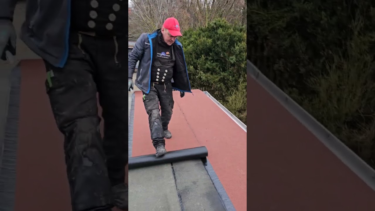 Flachdach mit PYE abdichten. Azubi klebt Schweißbahn in rot, anthrazit und grün. Nähte abgedtreut 