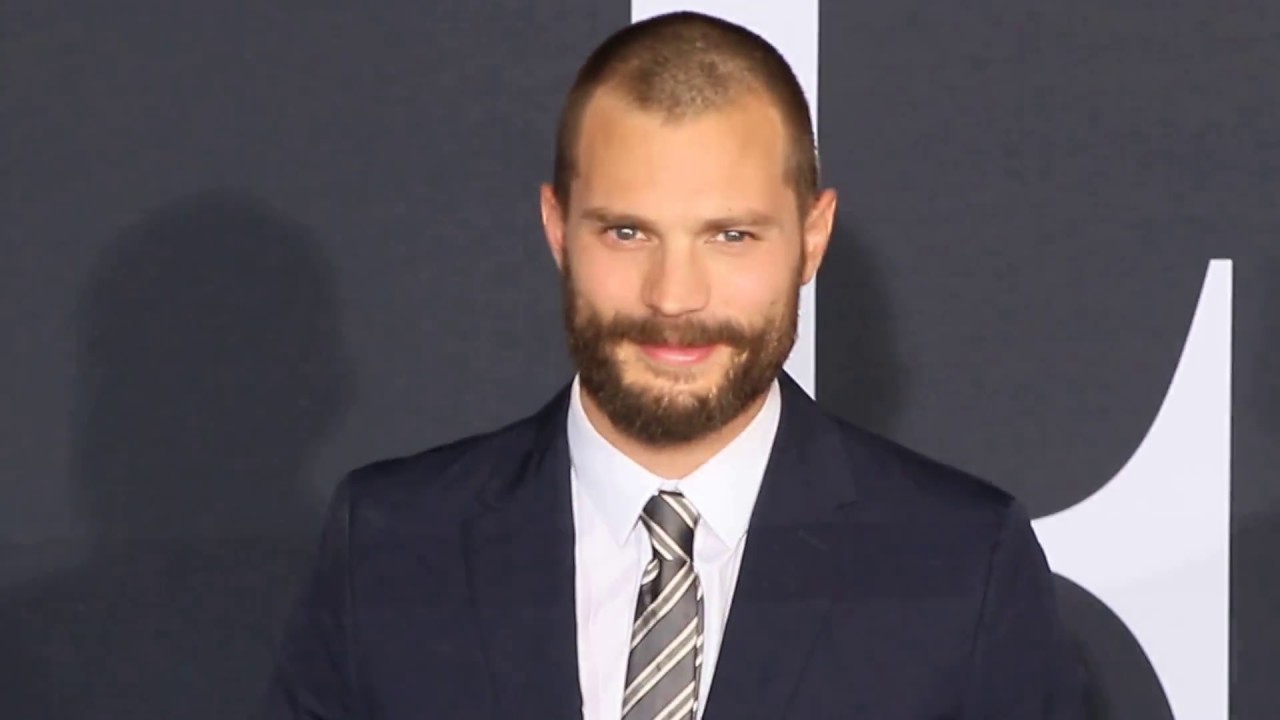 Jamie Dornan smiles with a black beard.