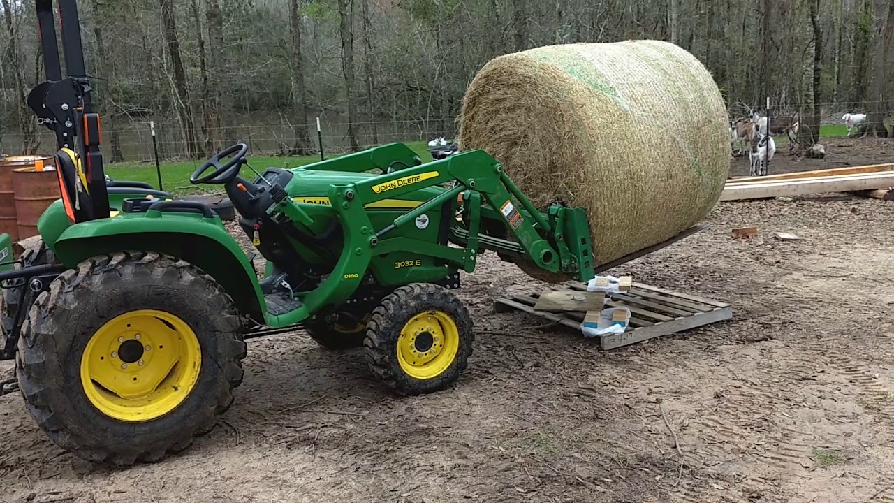 John Deere 3032E handling a round bale of hay
