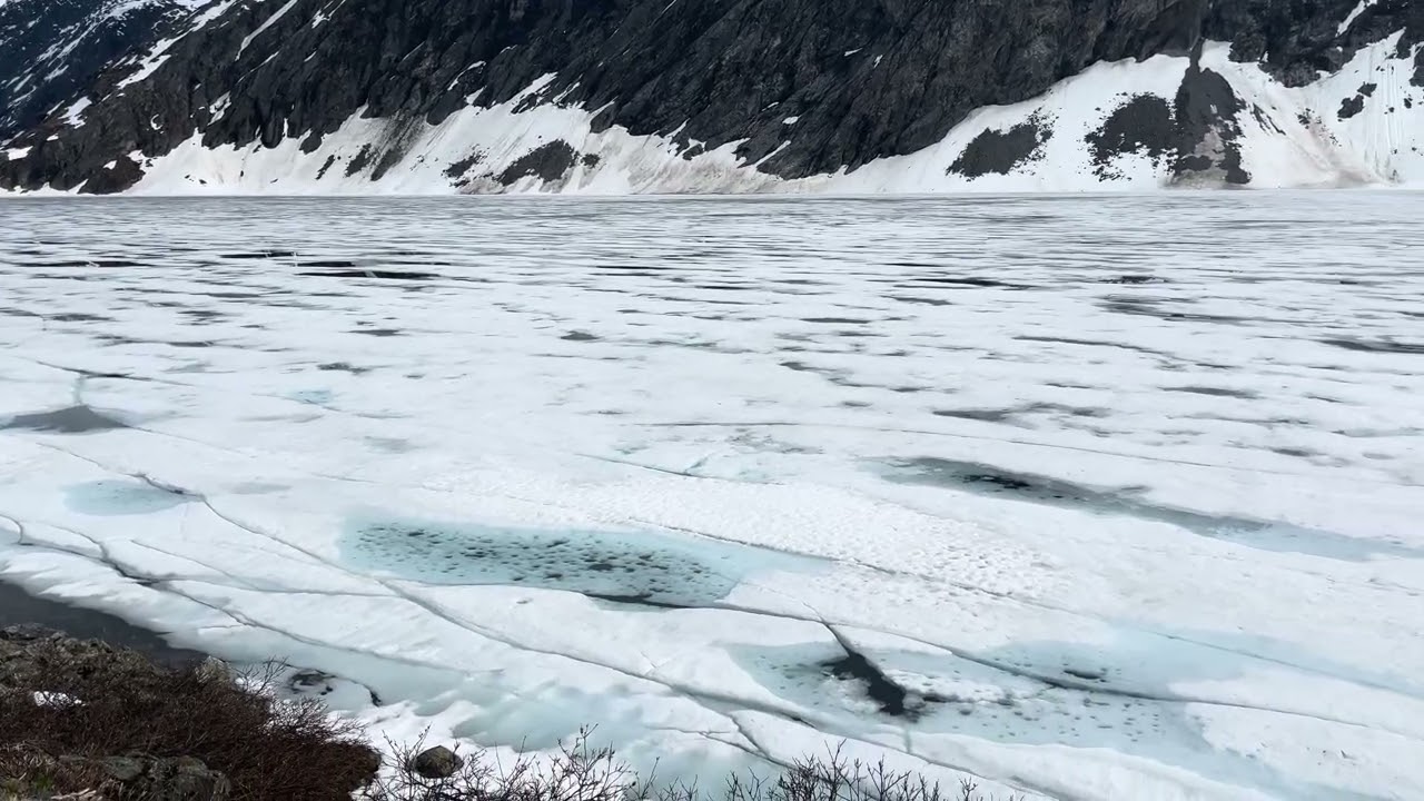 Big frozen lake and mountains with snow on it road to fjord