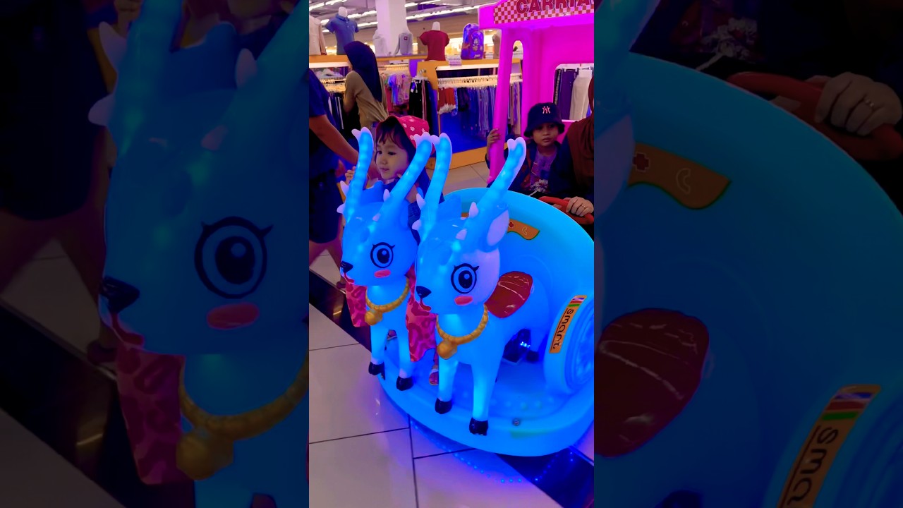 Adik pakai topi merah duduk di atas rusa putih wajah diantara dua tanduk panjang warna warni lucu