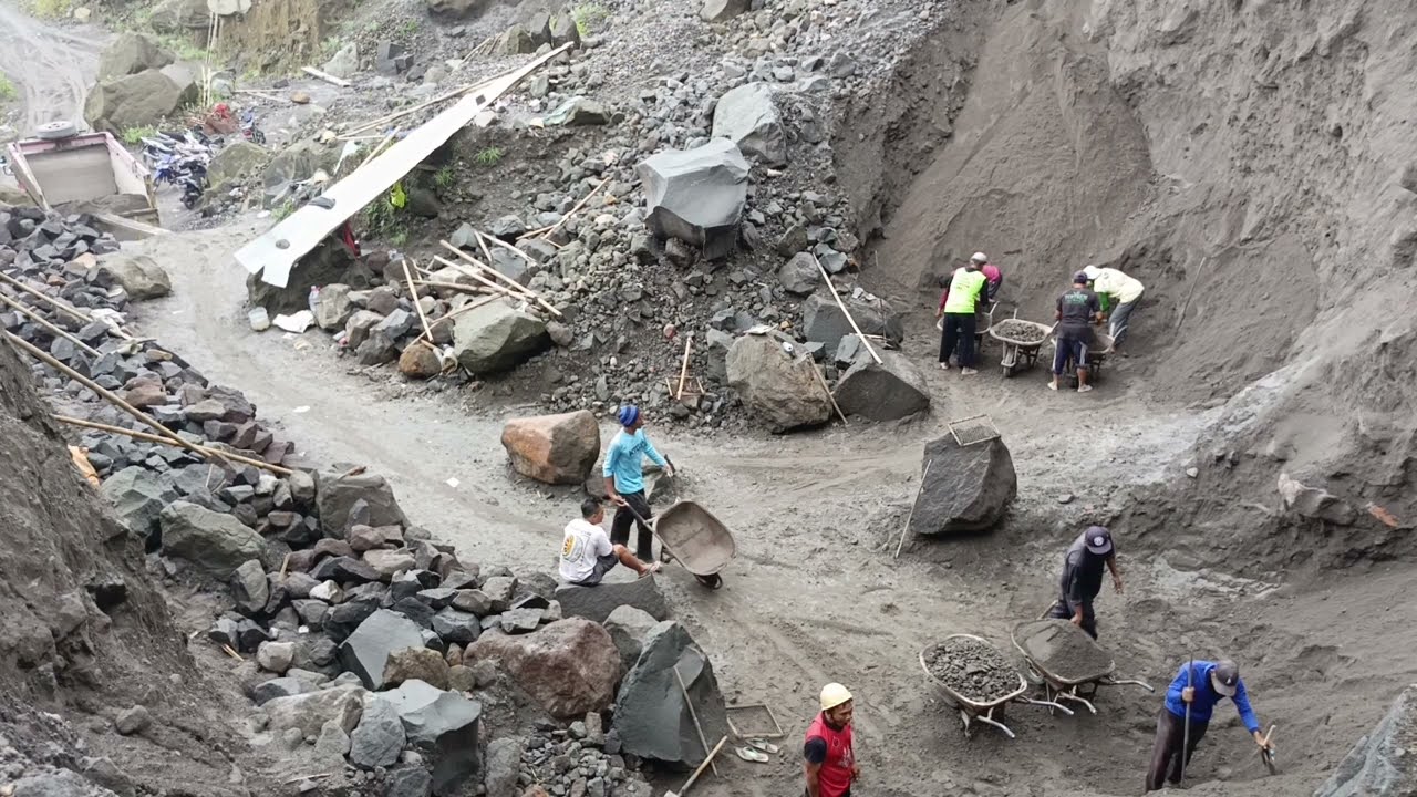 There is a large rock above the mine workers and they are working under it