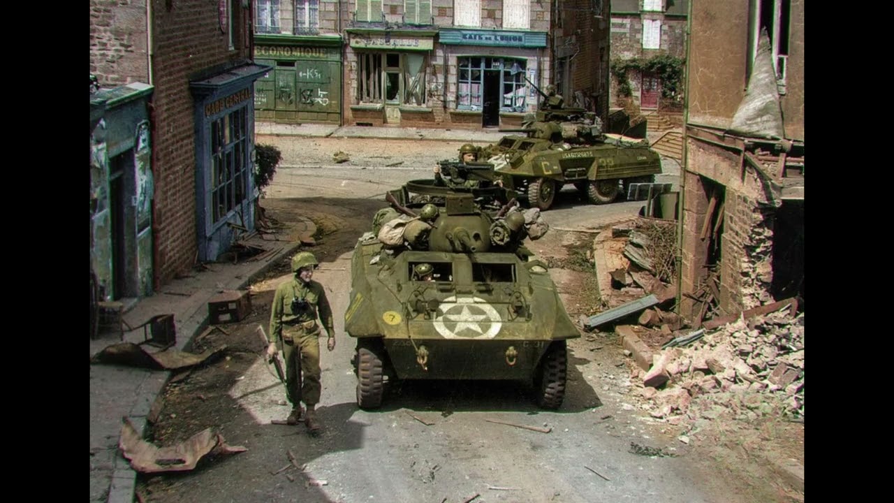 M8 “Greyhound” armored cars of the U.S.Reconnaissance Battalion turn onto Rue de la Forêt, Normandy.