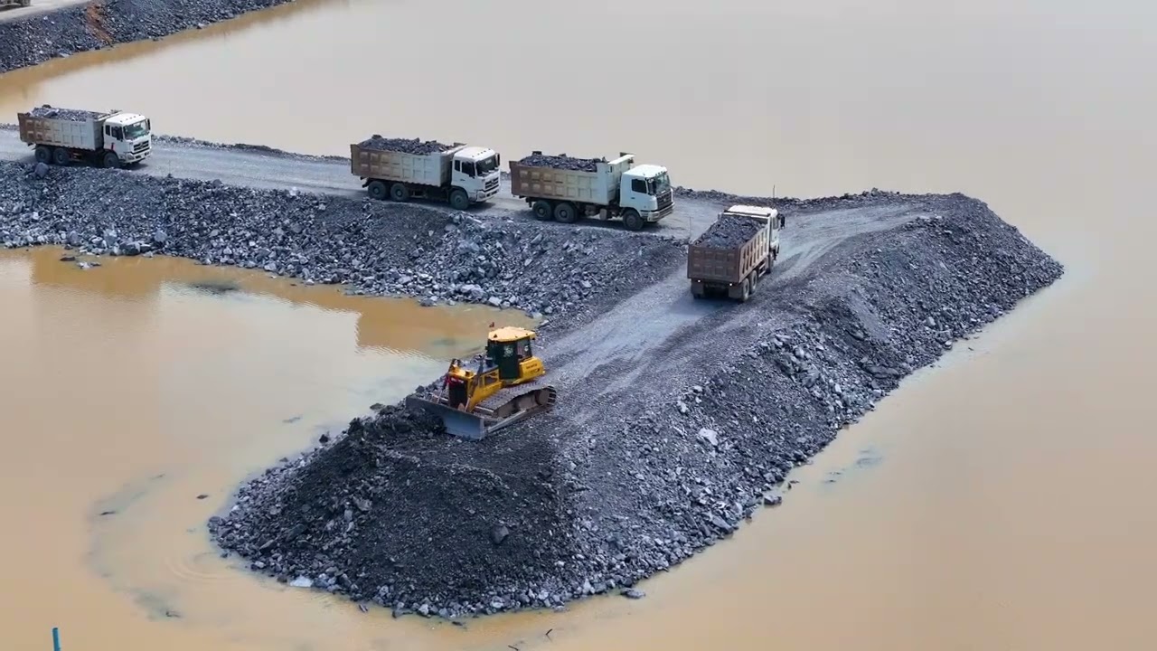 Excellent Road Project!Reclamation Project SHANTUI: Numerous dump trucks unloading stone and a dozer