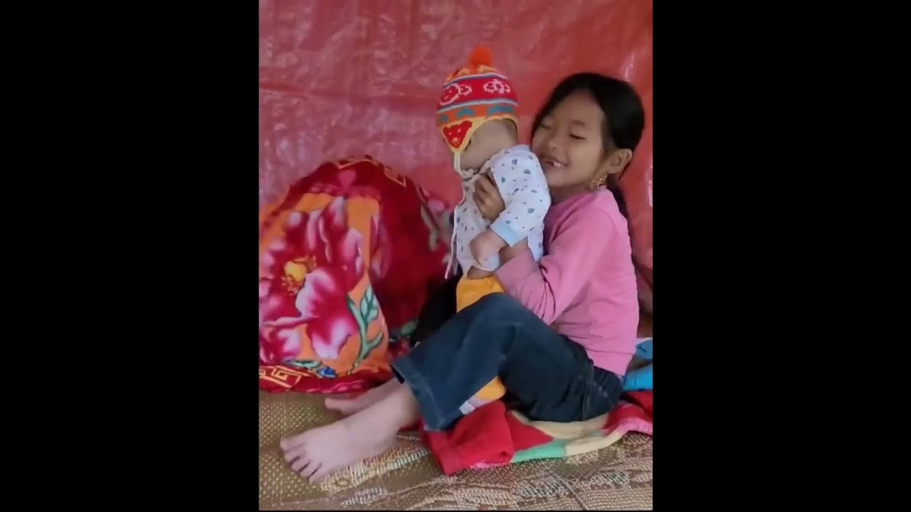 Two siblings cut small pieces of wood to build a door, lovingly caring for their little brother.