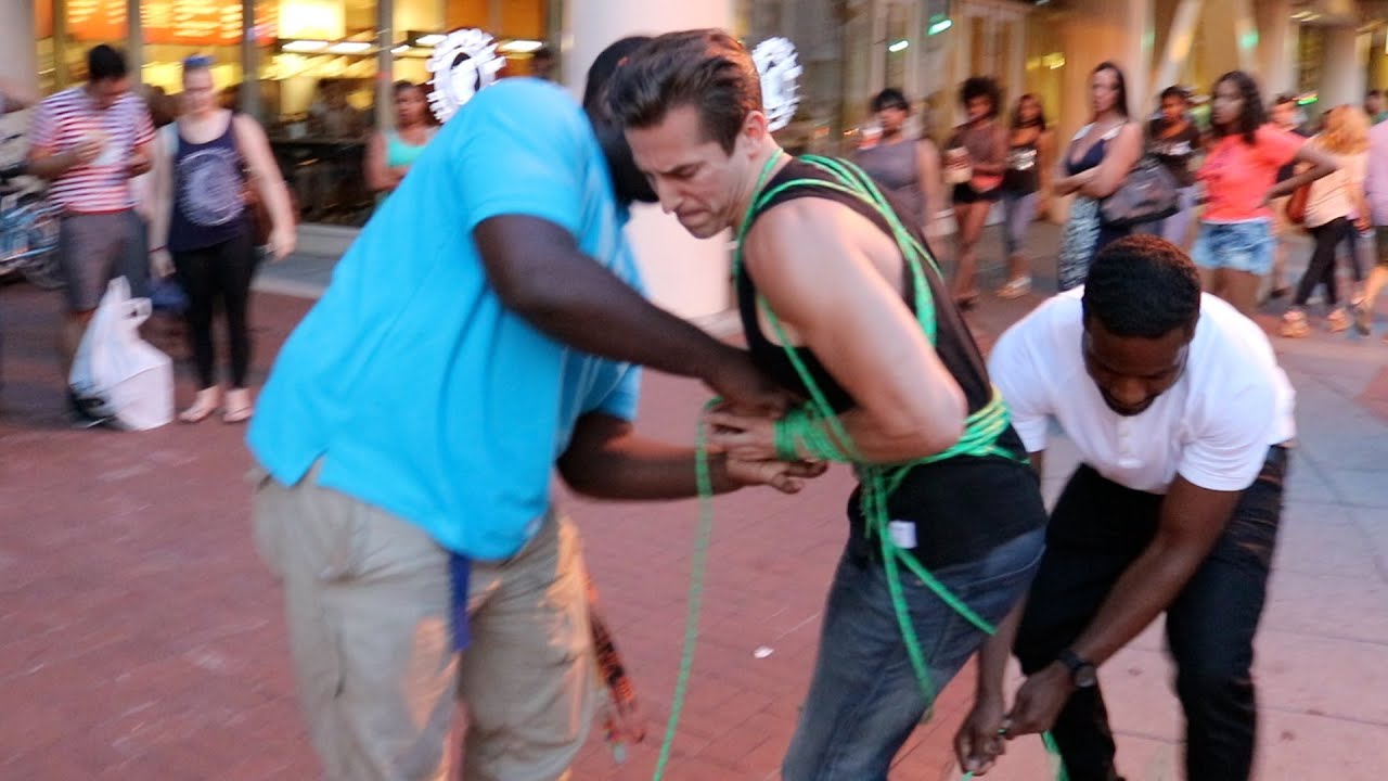 Two Guys Tie Up Man On Street While Police Watch
