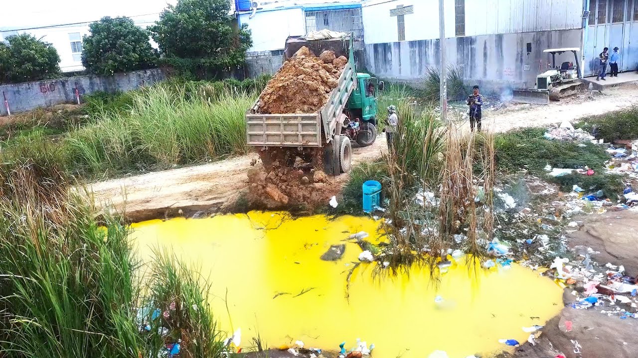 Small-scale machinery pushes soil & rock into deep water locations using multiple earthmoving truckស