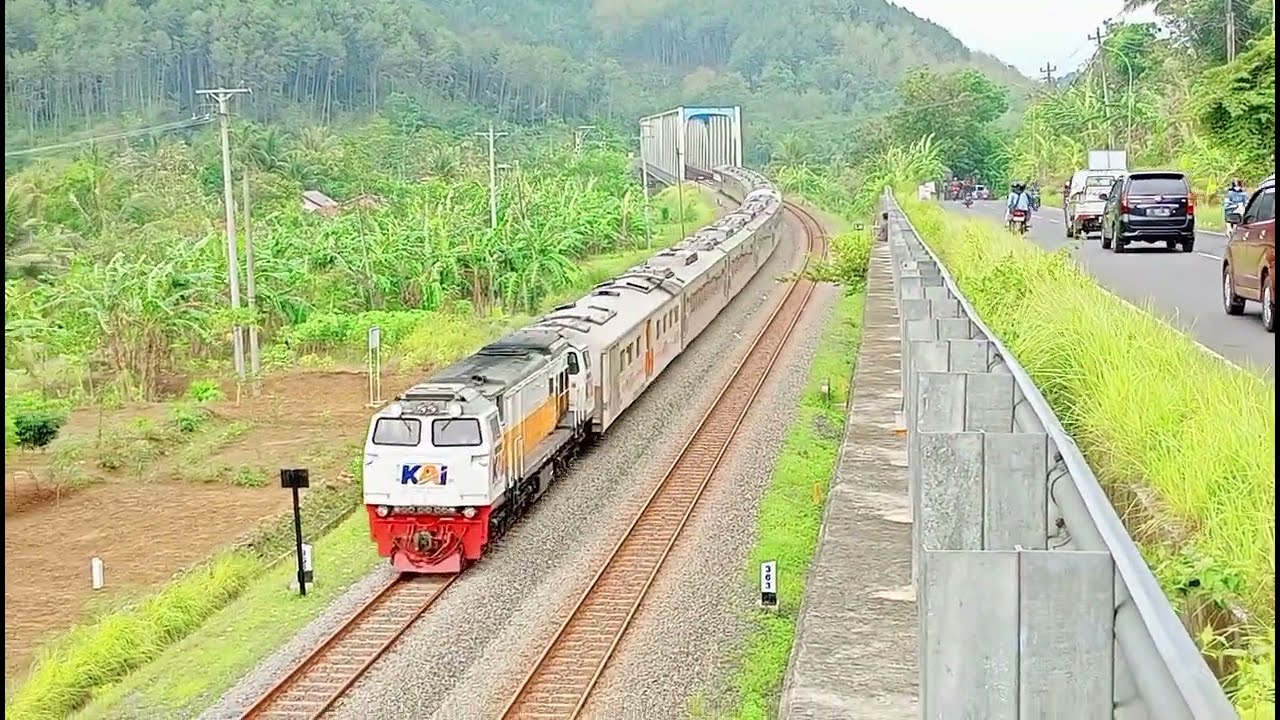 Kereta api panjang melintas di persawahan dan jembatan.