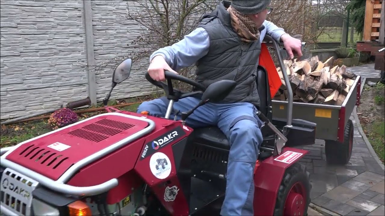 Traktor s hydropřevodovkou a vlečkou plnou dřeva couvá po chodníku