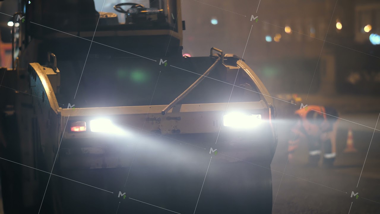 Road roller lays asphalt in the city. Road repair at night. Road workers are working in the