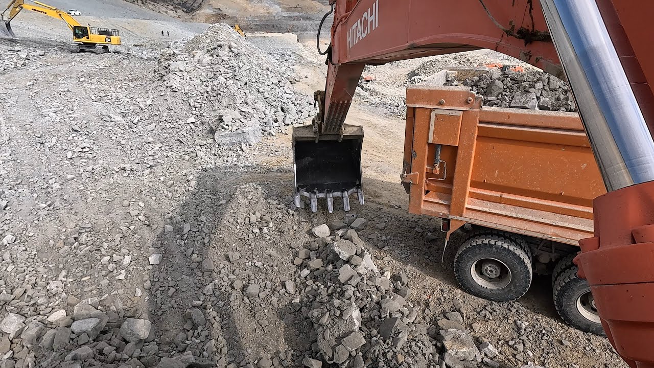 Экскаватор Hitachi Она грузит каменистые материалы в грузовики.