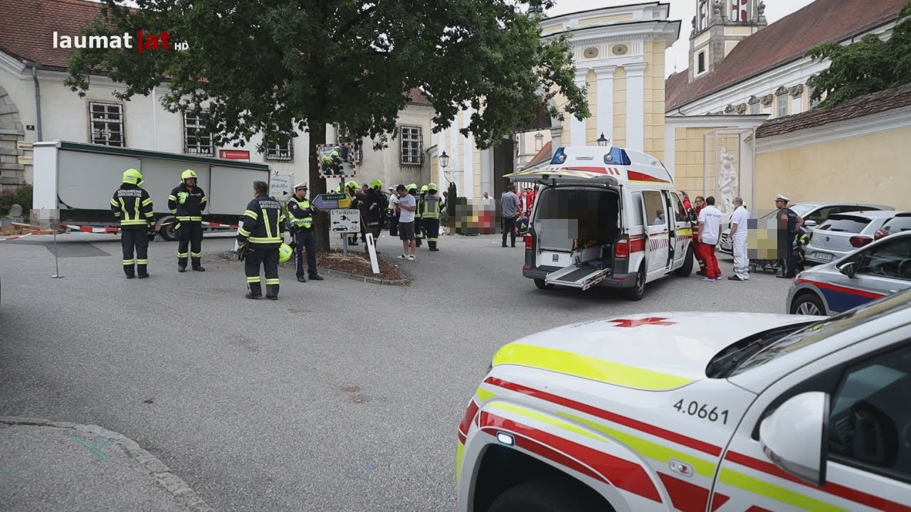 Auto fährt in St. Florian vor Stift in Personengruppe und Marktstand