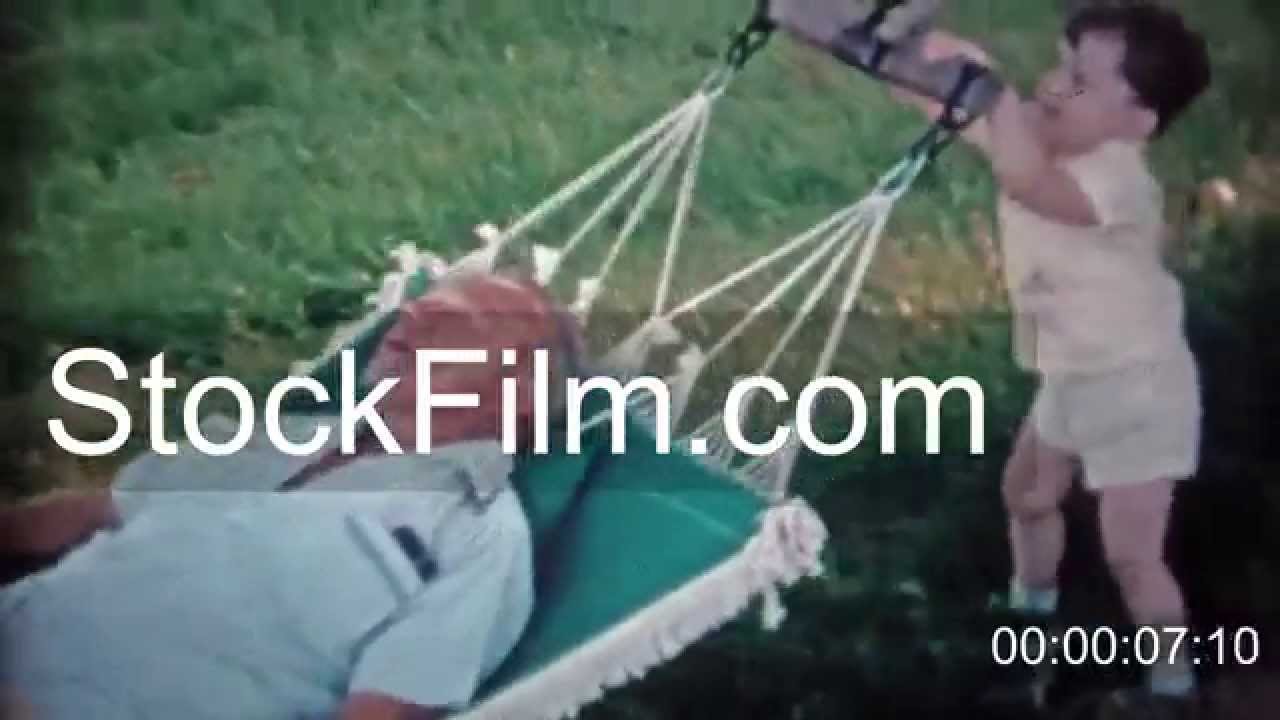 1966: Son rocking sleepy dad in outdoor summer hammock.  CHESAPEAKE BAY, MARYLAND