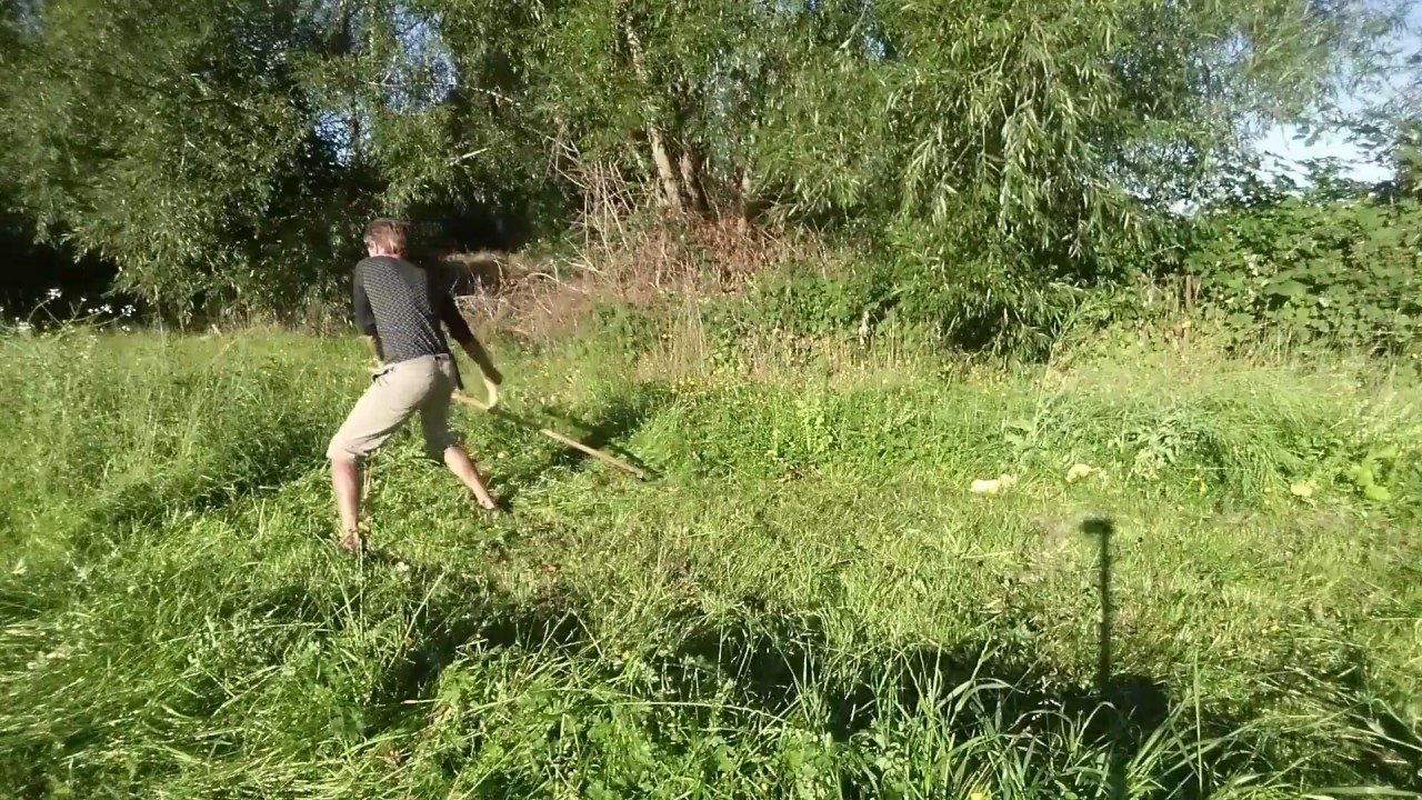 Scythe mowing tall vegetation on uneven ground.