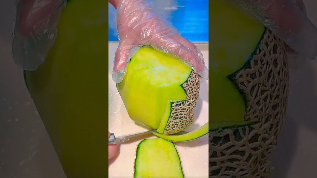 Peeling a large green cantaloupe with a knife on a white cutting board