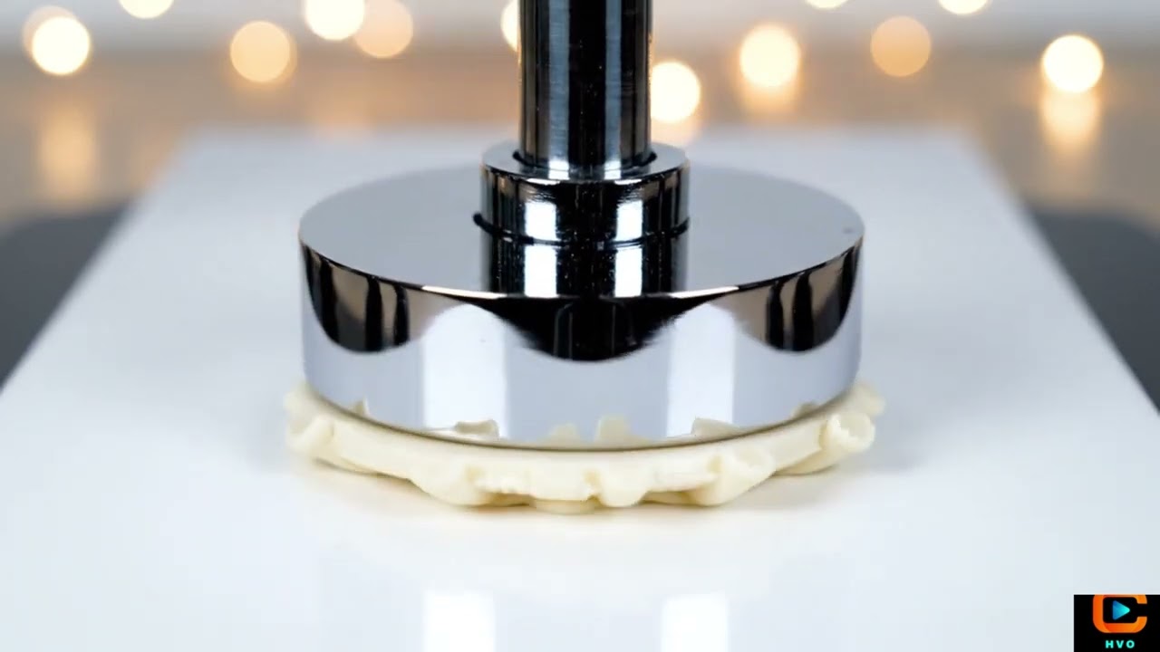 A polished chrome hydraulic press slowly descends onto a tiny, intricate wax castle.