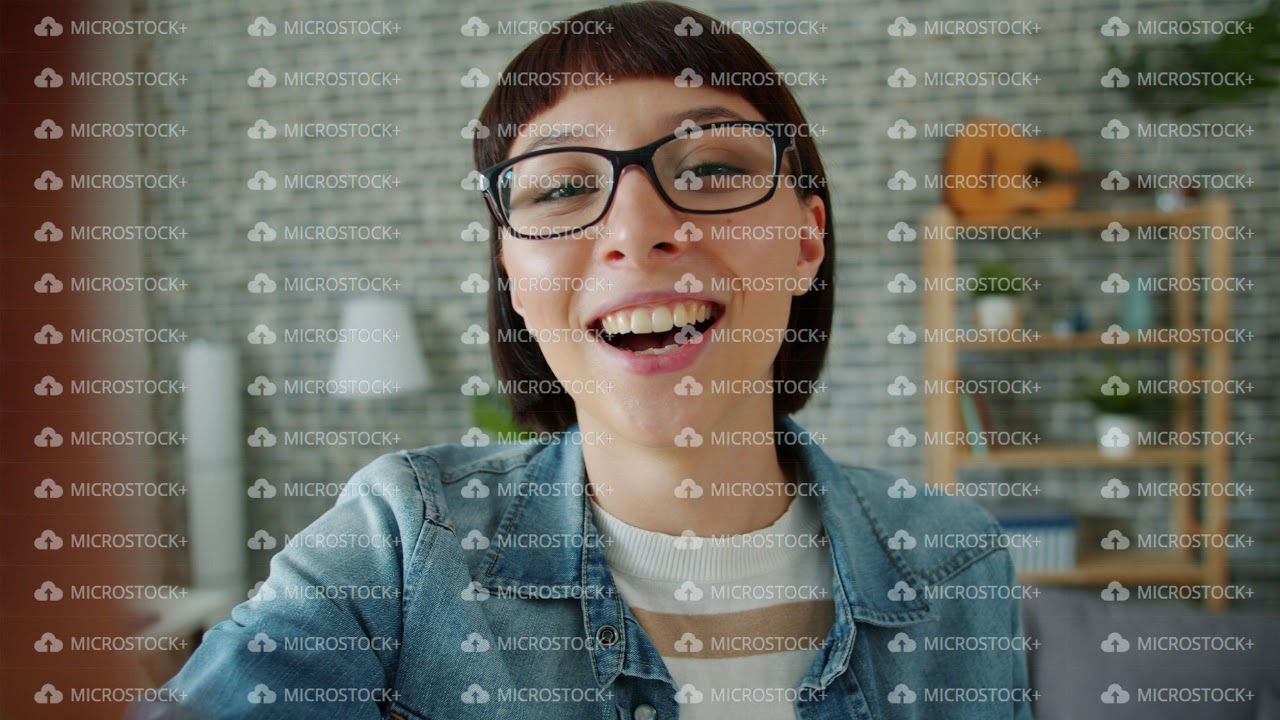 Young woman in glasses talking smiling looking at camera holding device at home