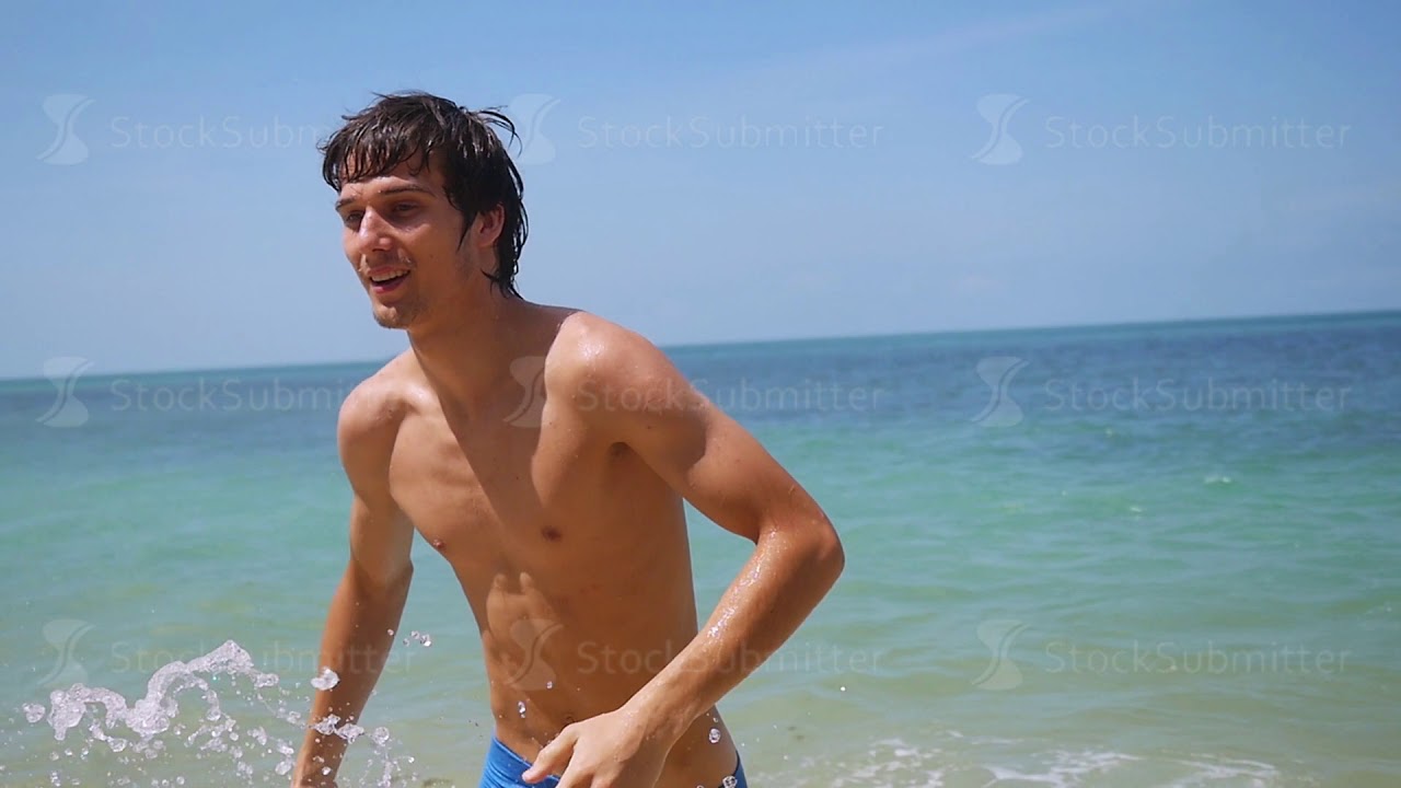 Young handsome happy man running on the beach from the sea at sunny day in slow motion. 1920x1080