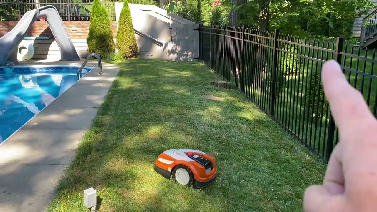 STIHL RMI 422 iMow robotic lawn mower installed in the backyard with pool, hill, and a few trees
