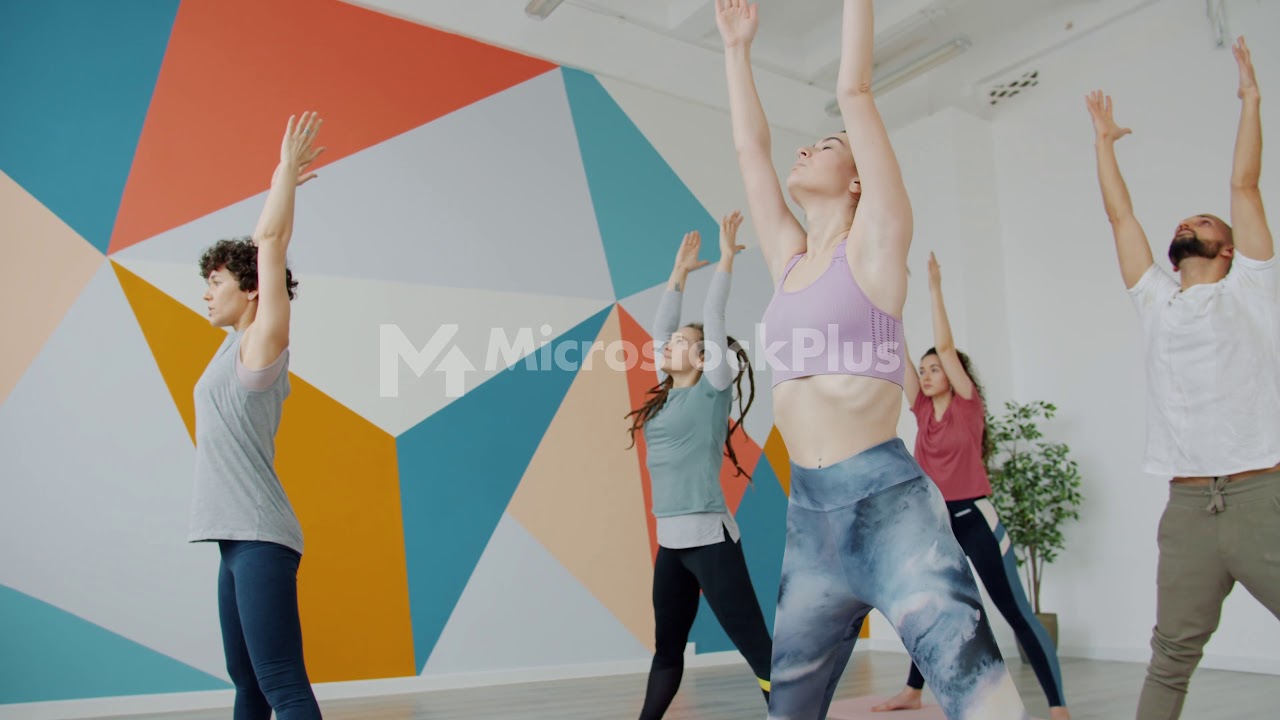 Girls and guy bending forward during yoga practice in spacious gym training together