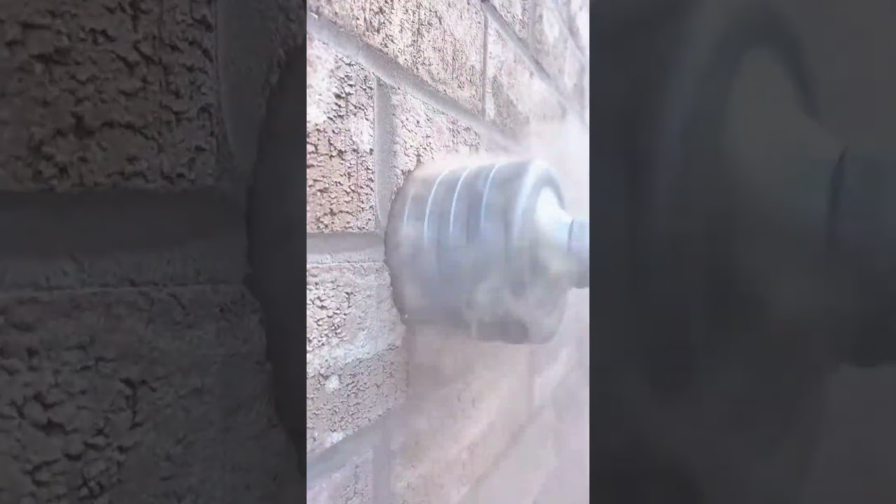 drilling a round hole automatically using a silver drill bit into a brown brick wall in an outdoor