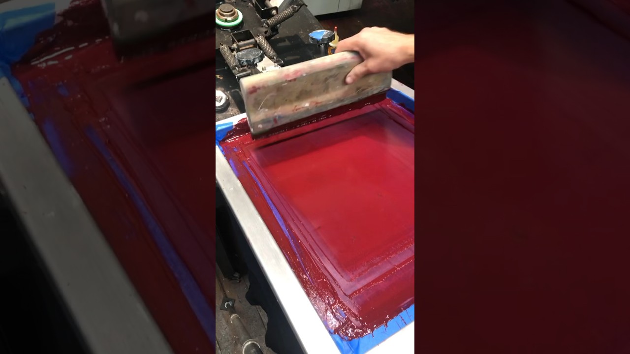 Screen printing a two color design on black tees by hand with water based inks.