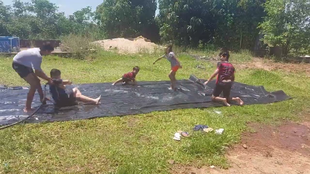 Crianças brincando de escorregar na lona com sabão...